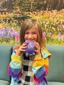 A six-year-old named Rory happily holds her purple Kitsap Credit Union piggy bank.